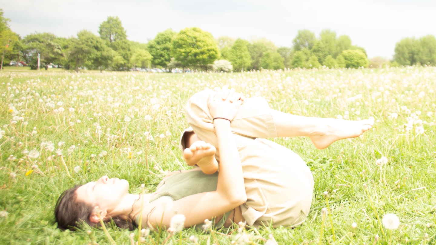 Training Ground (Spring 2021) Artist Emily Neale, lying legs crossed in a open green field