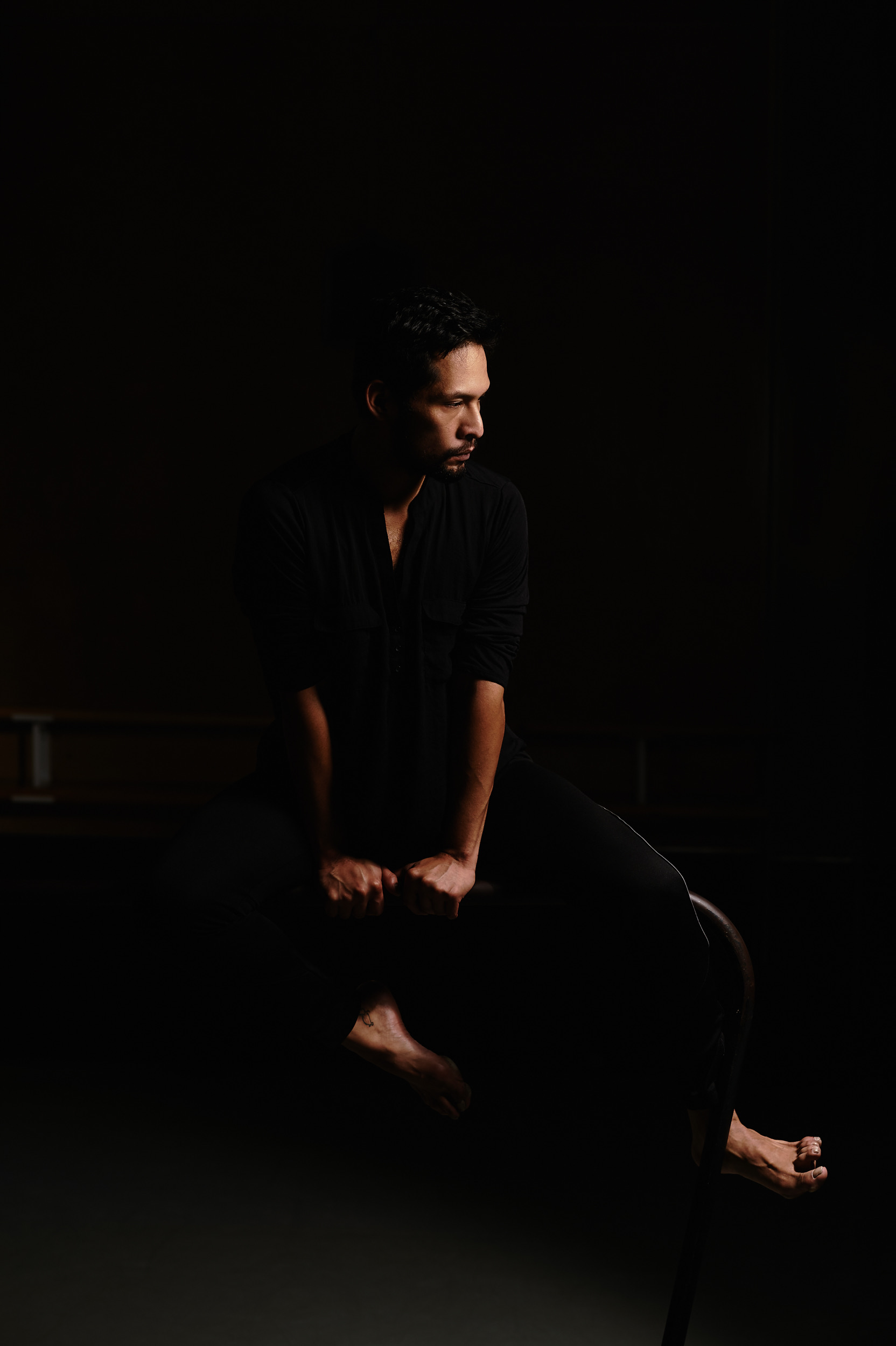 Victor Talledos seated on a stool, tension in toes, looking to the side