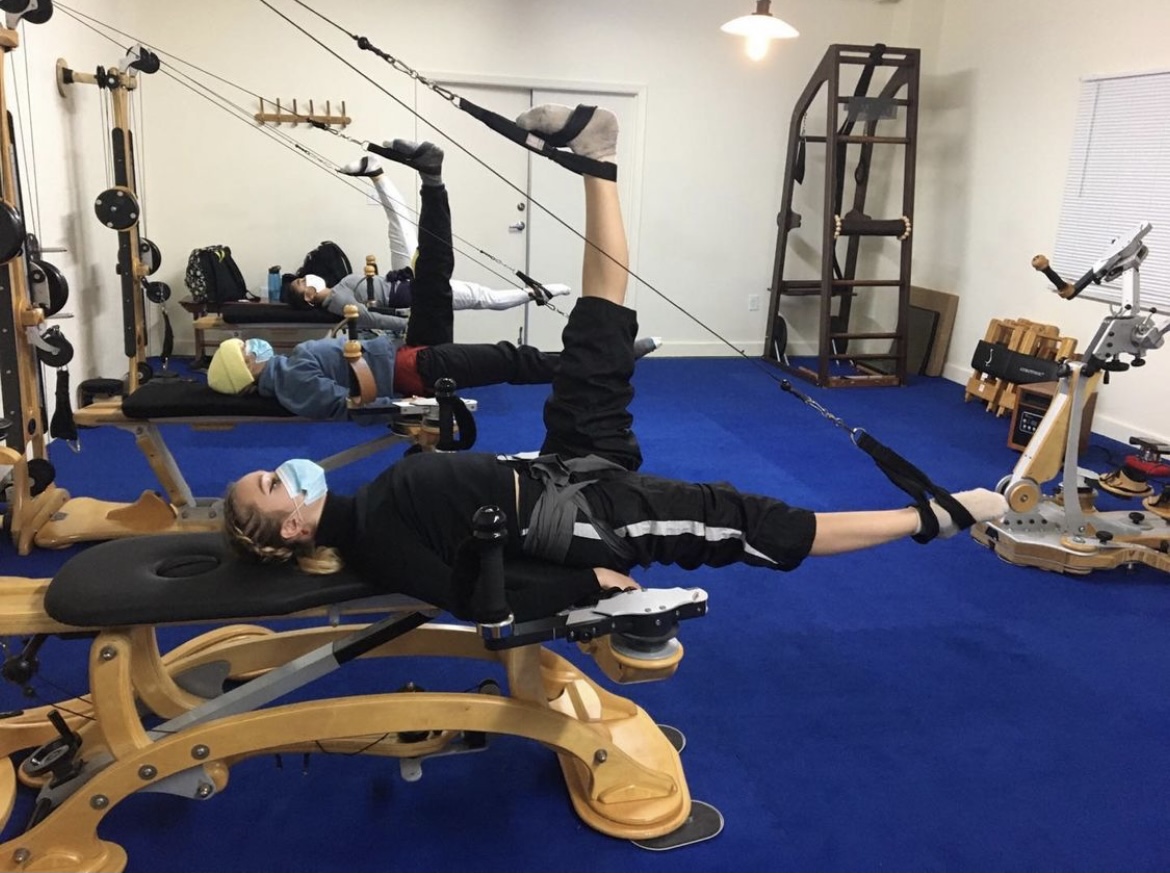 BFA at Dominican sophomores doing hamstring exercises on the GYROTONIC® Towers in San Francisco. All of the students are wearing masks.