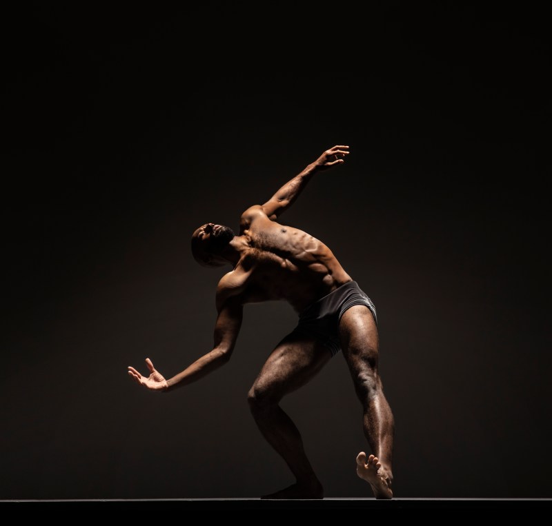 LINES Ballet company artist Babatunji Johnson with one leg outstretched and foot flexed, torso twisting upward while one arm extends out and other arm curves with hand open
