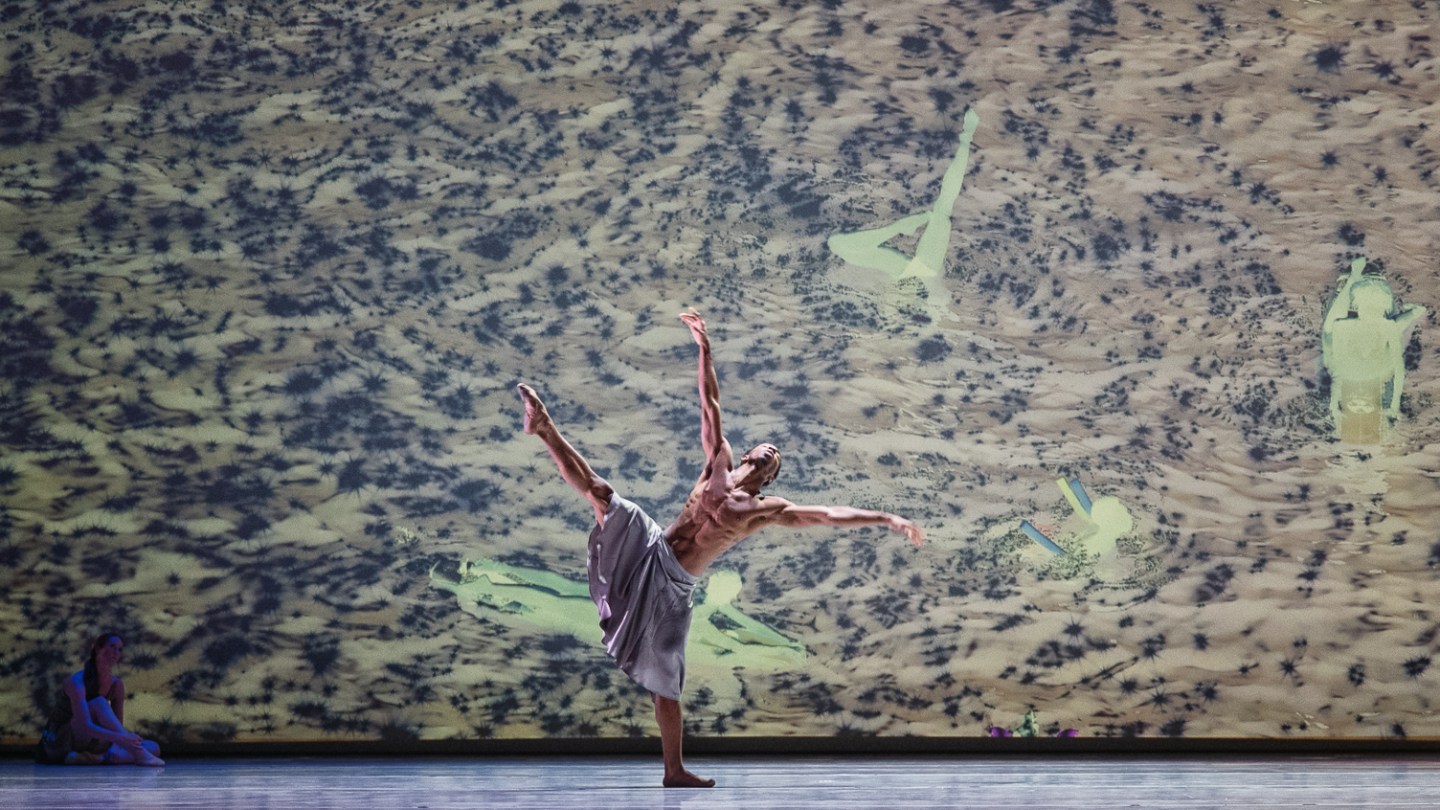 Josh Francique dancing on stage in Alonzo King's work titled "Let Not Your Heart Be Troubled" with a large-scale visual in background by photographer Richard Misrach