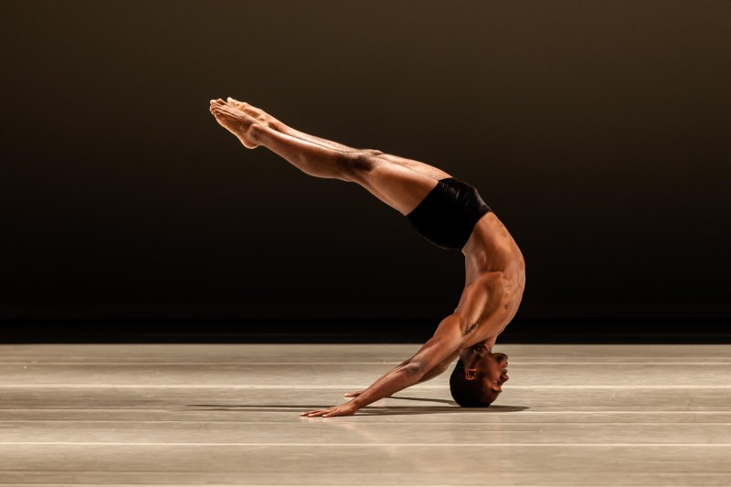 Babatunji as a LINES’ Training Program student performing on stage, balanced in an head stand, with back arched so that his hands and arms extend back behind his head; his body forms a backward C-shape