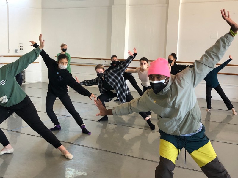 Babatunji dancing in a studio at LINES Dance Center with LINES Ballet Discovery Project students; all the dancers are wearing masks and Babatunji is wearing a hot pink beanie