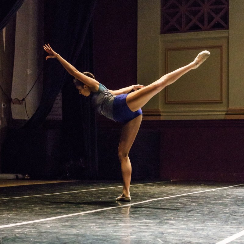 Zara Anwar performing on stage at Angelico Concert Hall on Dominican University of California's campus; Zara is in arabesque with her supporting leg in plié