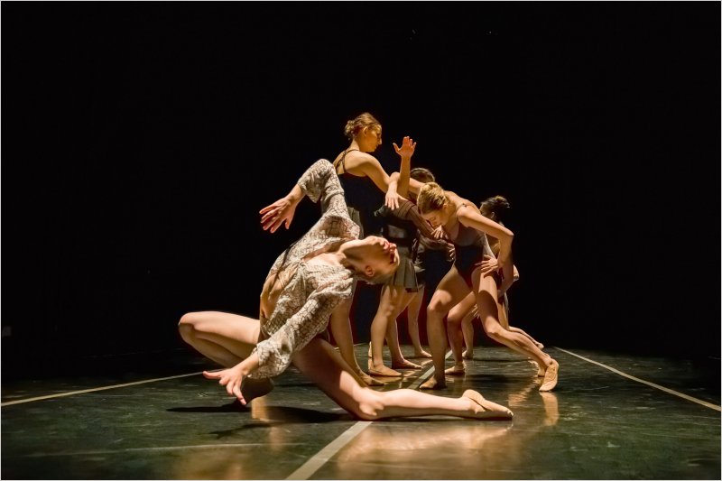 Emma Debski performing on stage at Angelico Concert Hall on Dominican University of California's campus; Emma is in a very deep lunge position arching her torso back; other BFA at Dominican dancers are in the background partnering