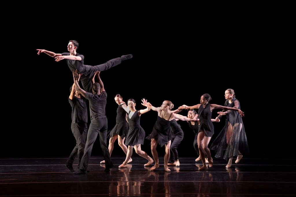 Summer Program student perform onstage, wearing all black costumes. One dancer is lifted by two others, followed by a group.